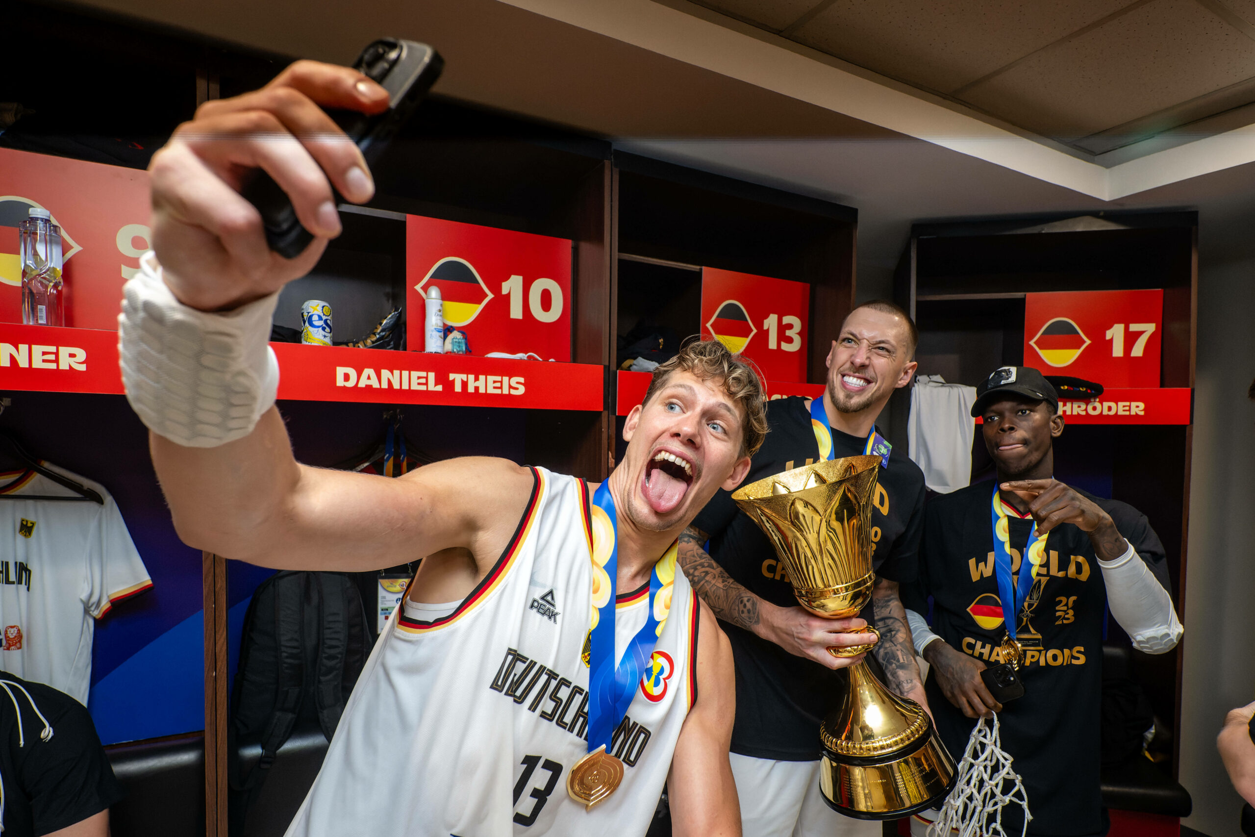 Moritz Wagner, Daniel Theis und Dennis Schröder posieren mit dem WM-Pokal für ein Selfie