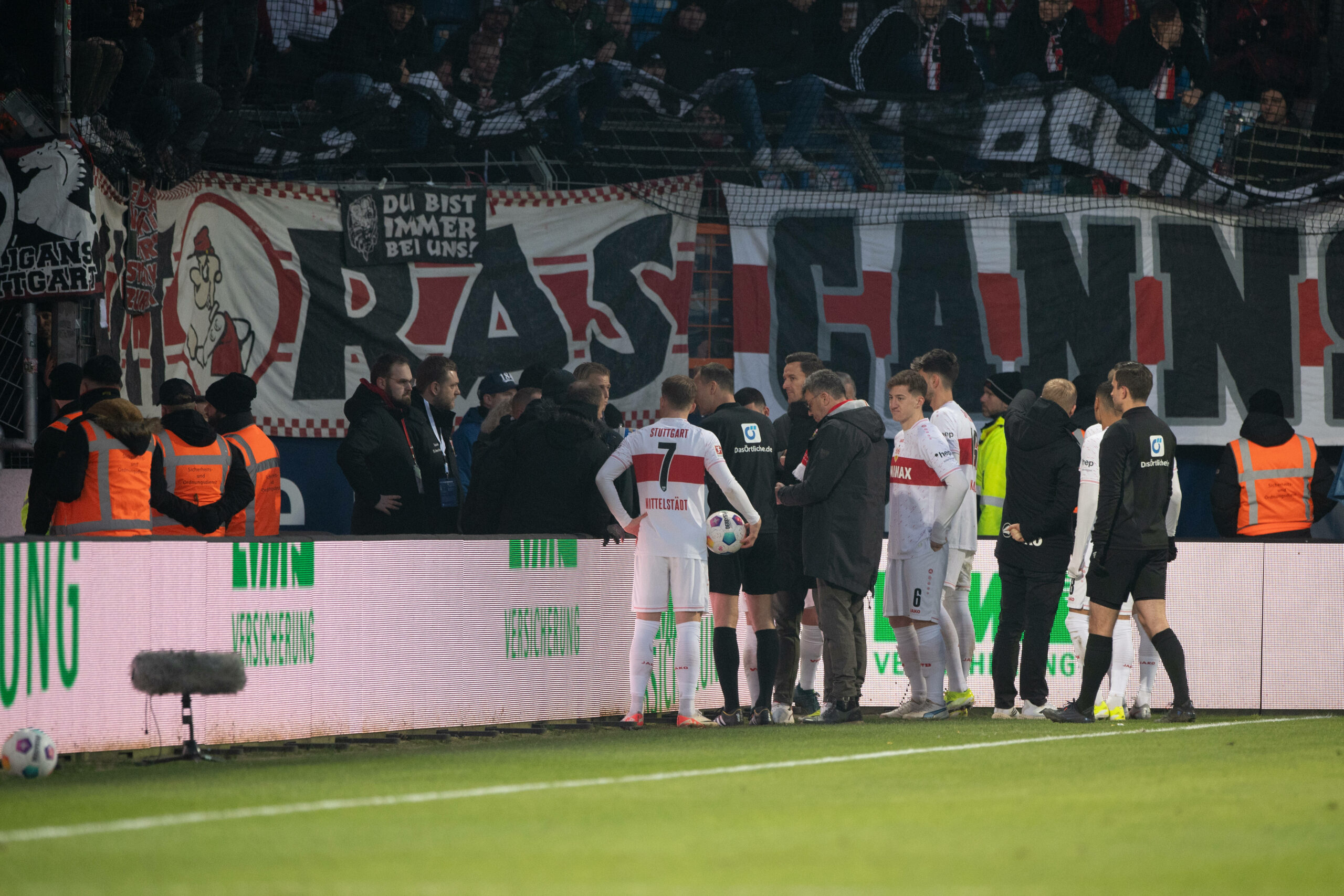 Spieler von Stuttgart stehen am Spielfeldrand um auf die Fans mit Bannern einzureden