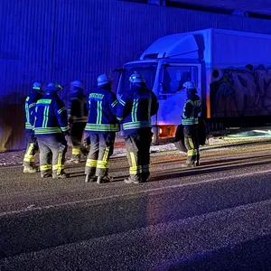 Ein Lkw steht nacht unter einer Autobahnbrücke in Stapelfeld. Links davon stehen Feuerwehrleute.