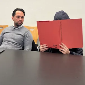 Der Angeklagte sitzt neben seinem Verteidiger und verbirgt sein Gesicht vor der Kamera.