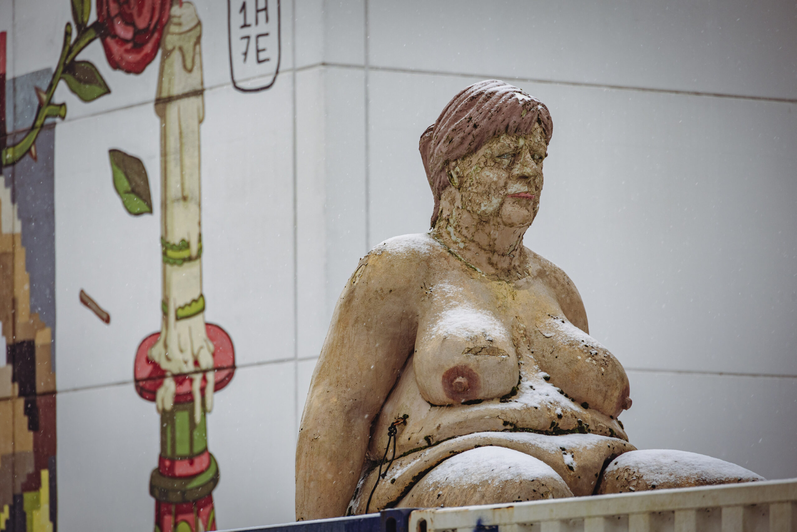 Eine sitzende, nackte Frau mit hängenden Brüsten, Schwabbelbauch und einem Gesicht, das stark an Angela Merkel erinnert