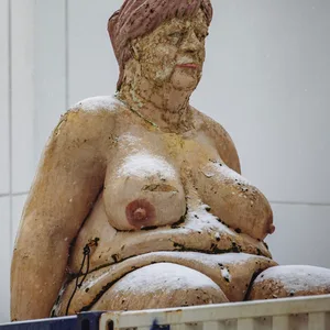 Eine sitzende, nackte Frau mit hängenden Brüsten, Schwabbelbauch und einem Gesicht, das stark an Angela Merkel erinnert