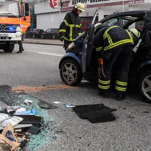 Feuerwehrmänner haben den Smart wieder aufgerichtet, auf der Straße liegen viele Dinge aus dem Innenraum des Autos.