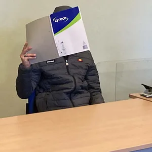 Der Angeklagte (r.) neben seiner Dolmetscherin im Gerichtssaal. Er verdeckt sein Gesicht mit einem Aktenordner.