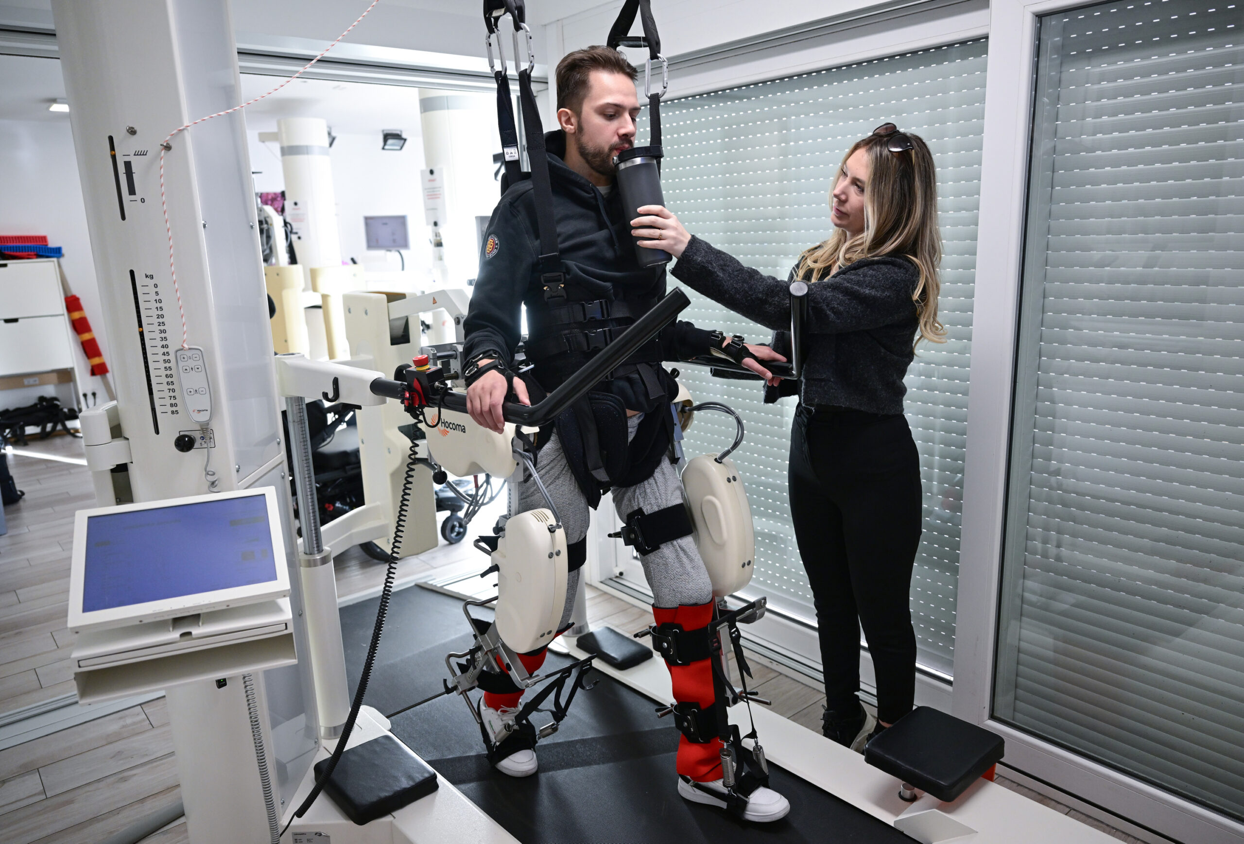 Der ehemalige Eishockeyspieler Mike Glemser absolviert in einer Reha eine Übungseinheit bei einer Robotergestützten Gangtherapie. Rechts seine Freundin und Stütze Lara Lindmayer.