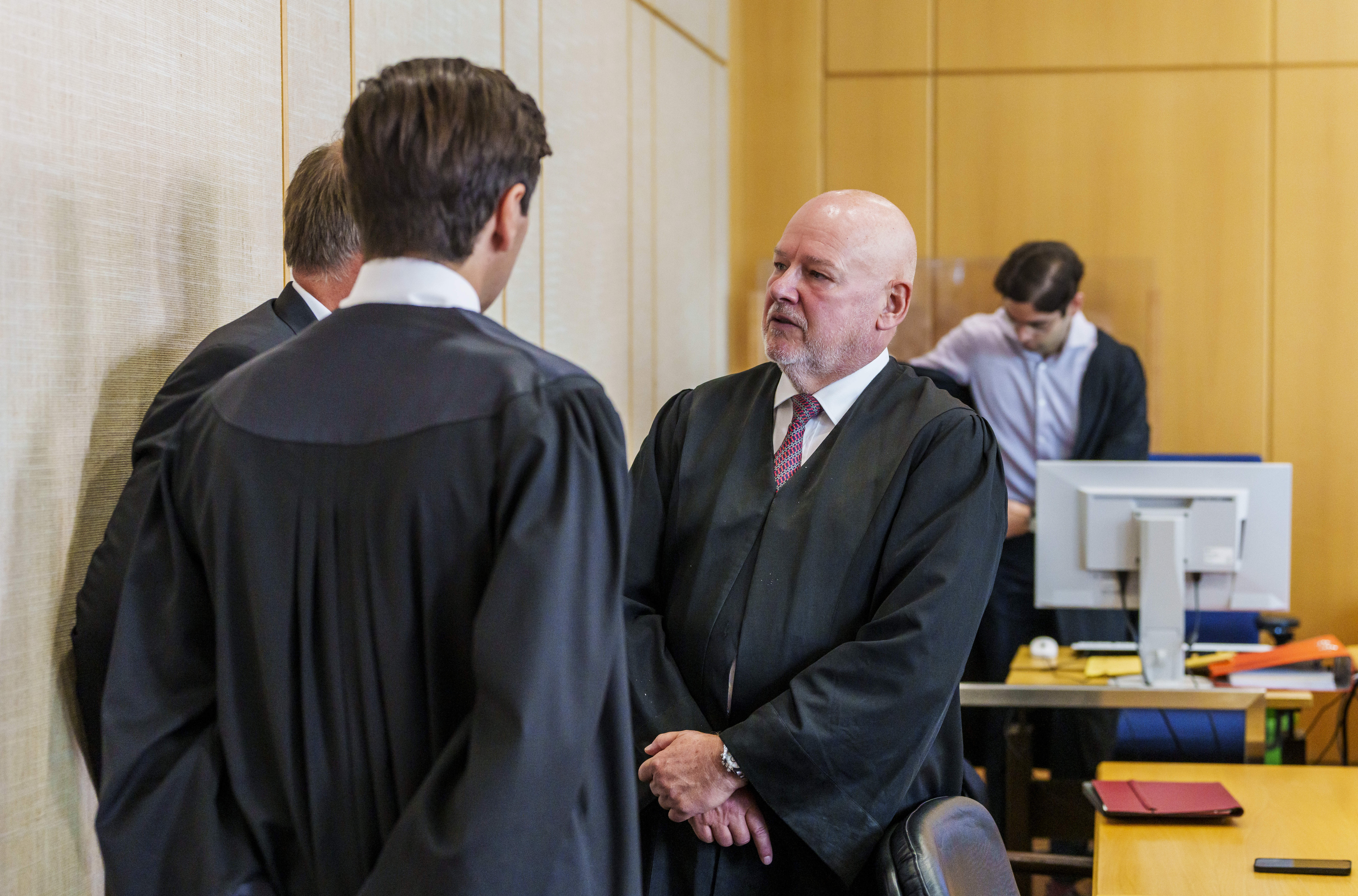 Der Angeklagte (l., verdeckt) steht vor beim Prozessauftakt mit seinem Anwälten im Gerichtssaal zusammen.