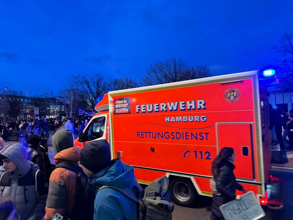 Ein Rettungswagen bahnt sich seinen Weg auf der Großdemo in Hamburg. Drum herum stehen Demonstranten.