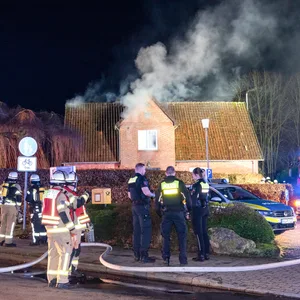 Einsatzkräfte stehen vor dem Haus, aus dem Rauch kommt.
