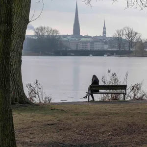 Eine Frau sitzt auf einer Bank an der Außenalster, der Himmel ist bedeckt.