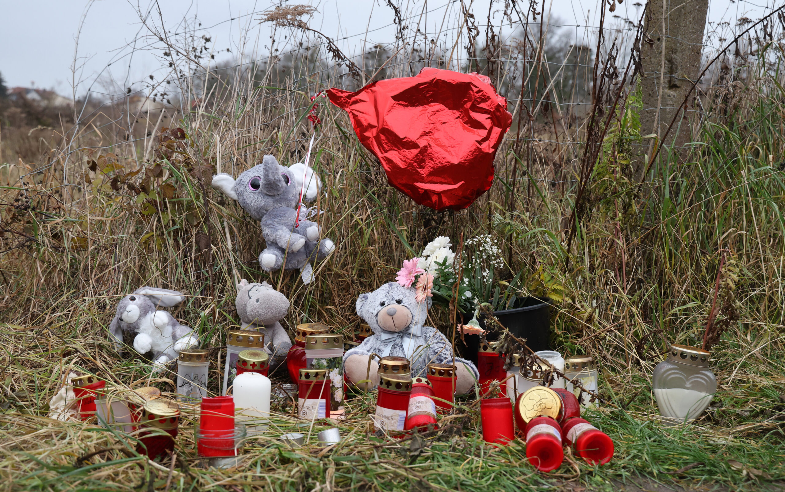 An einem Zaun zum verwilderten Grundstück, wo am 7. Dezember die getötete 18-jährige gefunden wurde, stehen Kerzen, Plüschtiere und Blumen. (Archivbild)