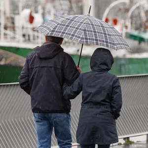 Ein Paar geht mit einem Regenschirm auf dem Hochwasserschutzbauwerk Baumwall spazieren.