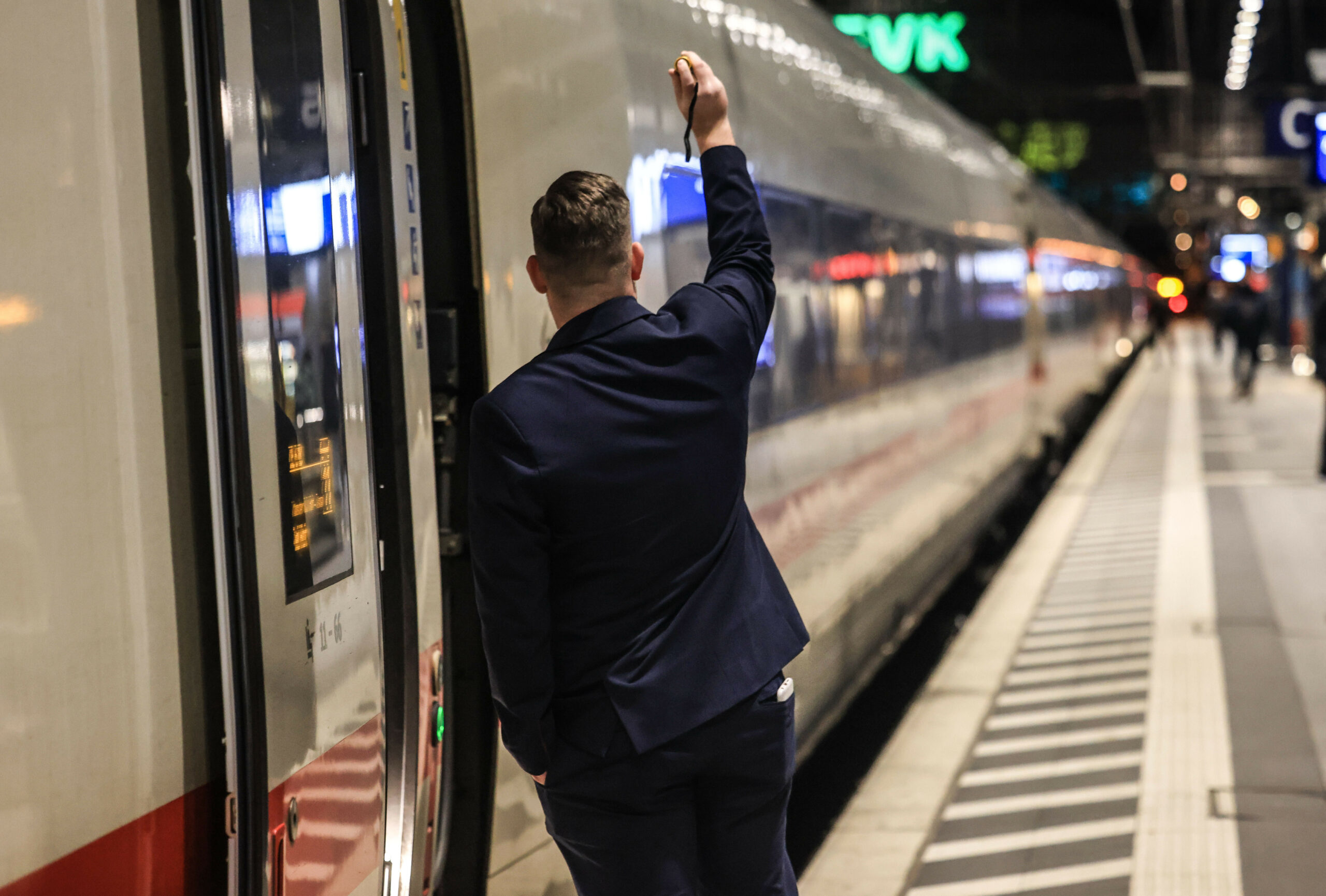 Ein Zugbegleiter gibt das Signal zur Abfahrt: Die Deutsche Bahn plant, viele neue Mitarbeiter*innen einzustellen.