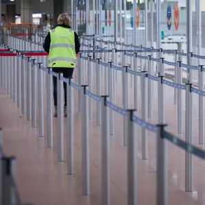 Eine Flughafenmitarbeiterin geht durch die geschlossene und menschenleere Sicherheitskontrolle im Flughafen Hamburg.