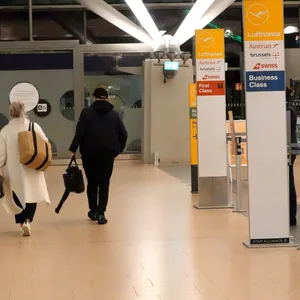 Reisende laufen im Terminal 2 an Schildern vorbei, die auf den Check-In-Bereich der Lufthansa hinweisen