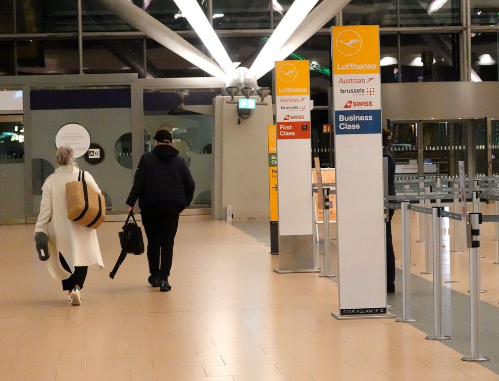 Reisende laufen im Terminal 2 an Schildern vorbei, die auf den Check-In-Bereich der Lufthansa hinweisen