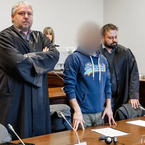 Der Angeklagte steht im Gerichtssaal zwischen seinen Anwälten.