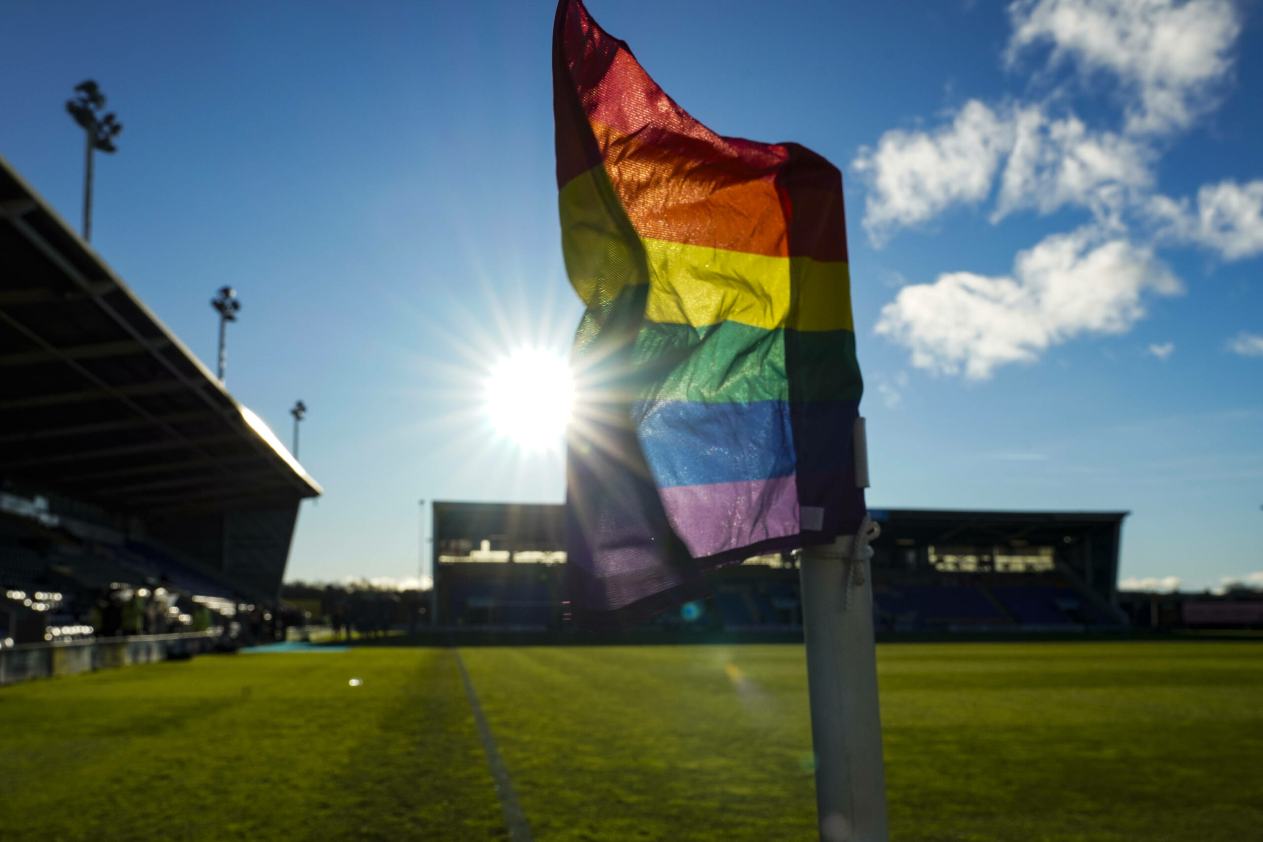 Eine Eckfahne mit Regenbogen-Flagge wird von der Sonne angestrahlt.