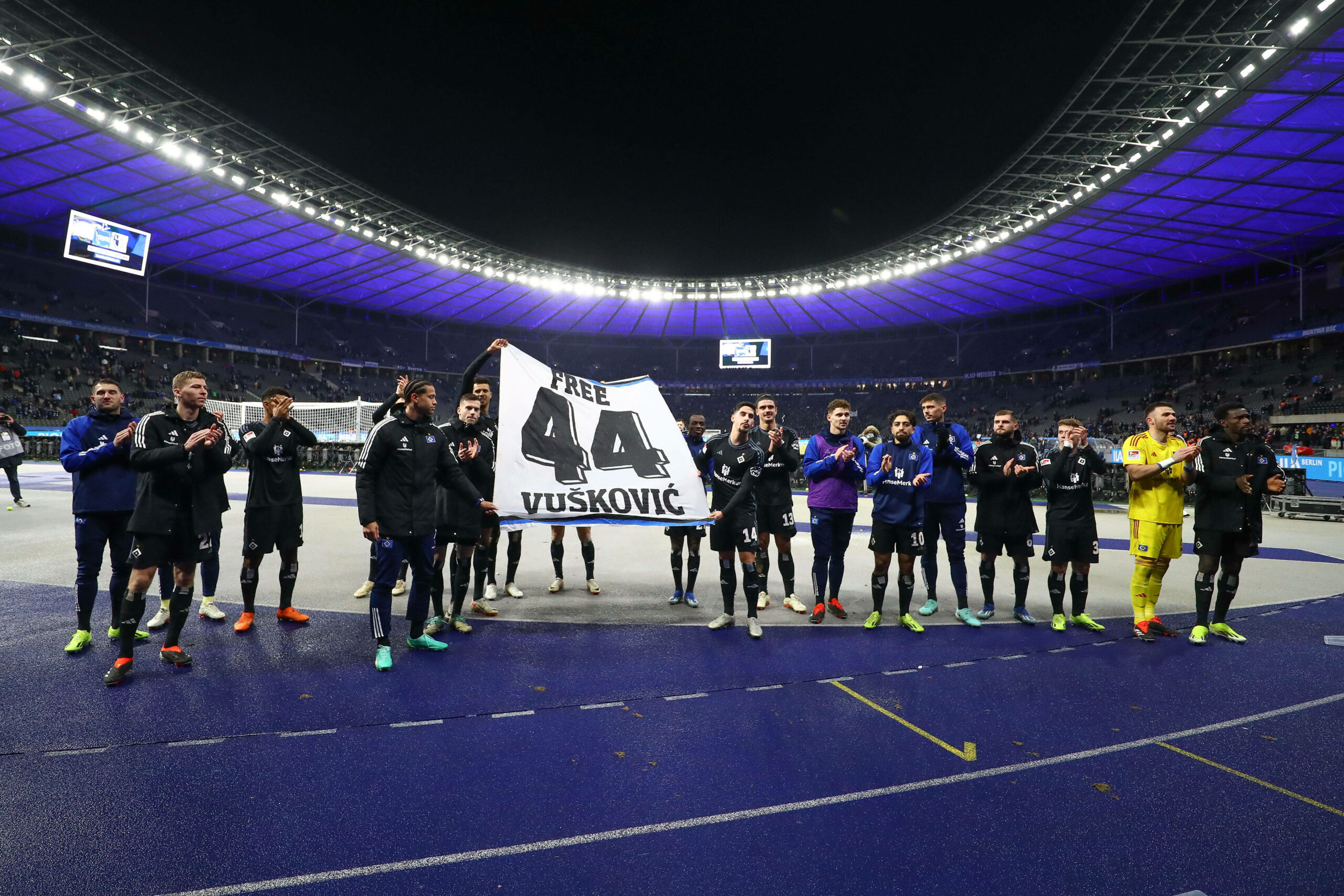 Die Spieler des HSV halten ein Banner mit der Aufschrift „Free Vuskovic“ Richtung eigener Fankurve hoch.