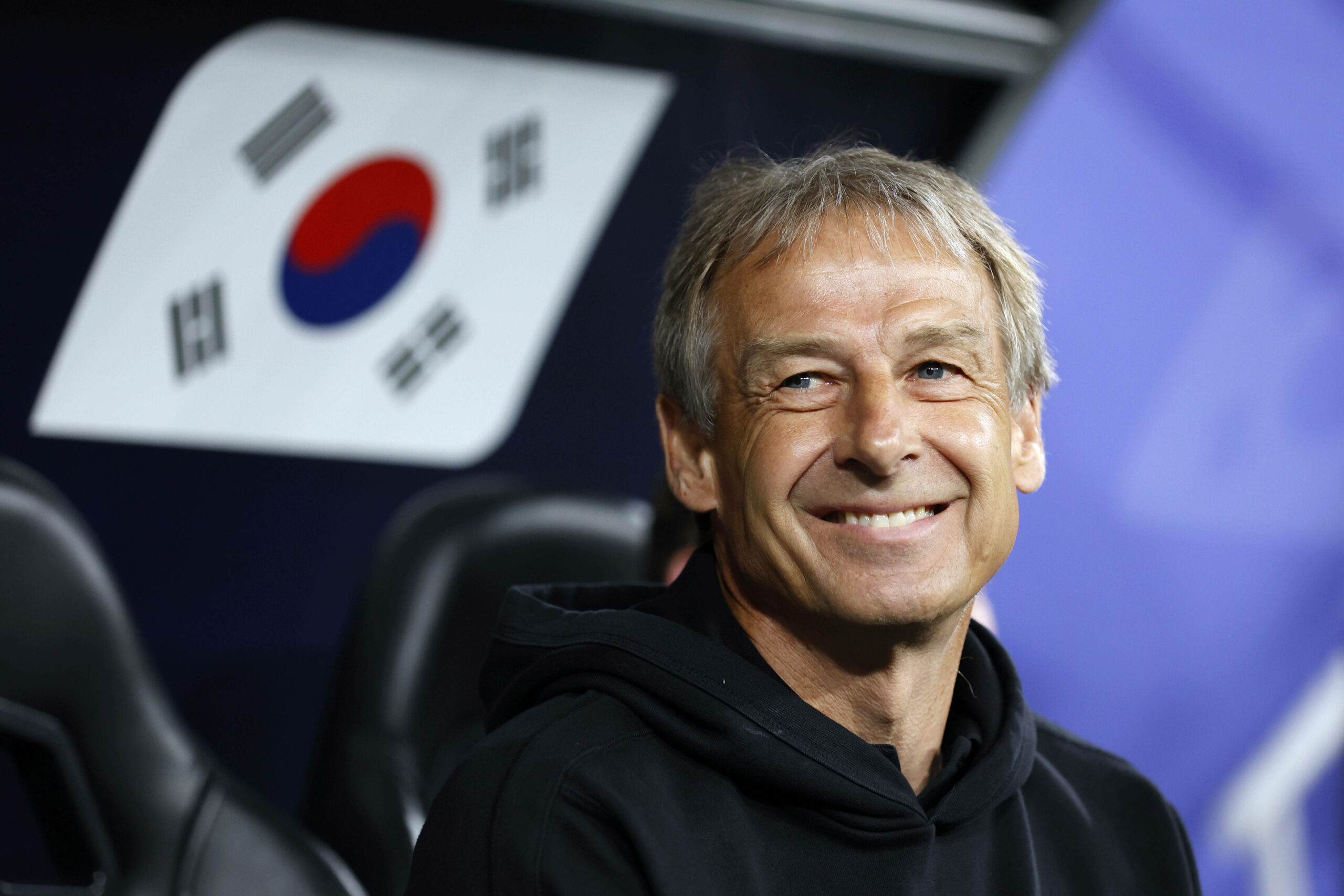 Jürgen Klinsmann sitzt auf der Bank und lächelt während sein Team verliert.