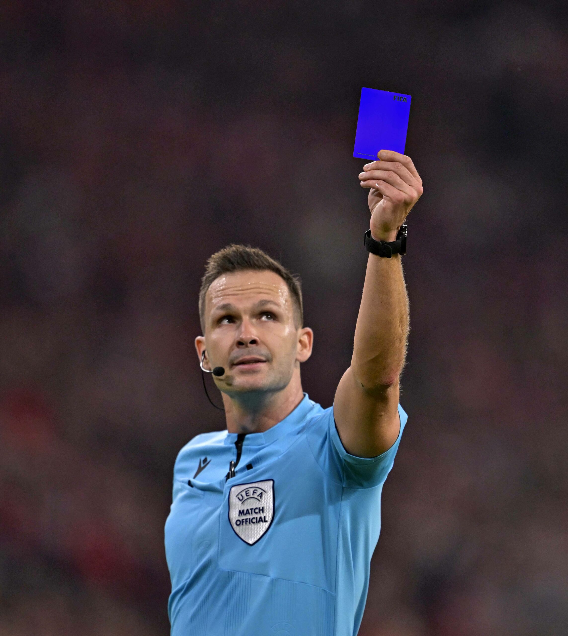 Ein Schiedsrichter hält eine blaue Karte in die Höhe.