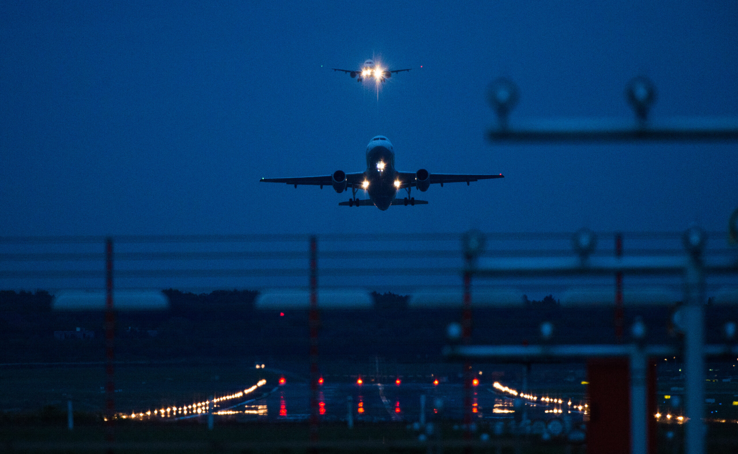 Ein nächtlicher Start am Hamburger Flughafen. Im Hintergrund setzt ein Flugzeug zur Landung an.
