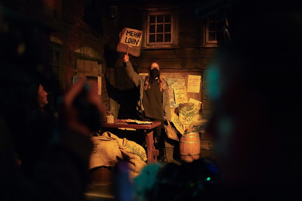 Eine Frau hält vermummt ein Plakat in die Höhe. Mindestlohn steht darauf