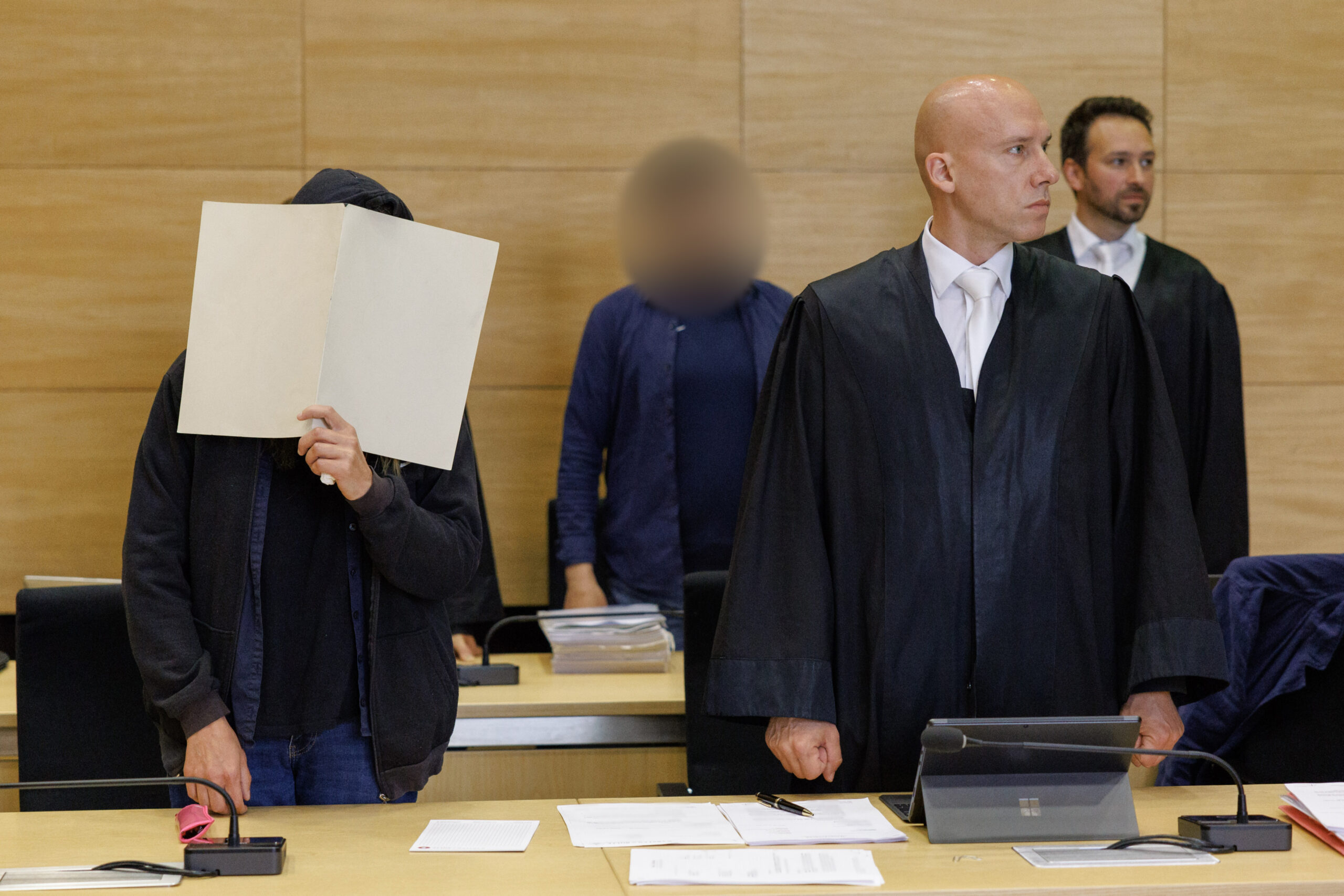 Die Angeklagten stehen zu Prozessbeginn mit ihren Verteidigern im Gerichtssaal des Landgerichts Bielefeld.