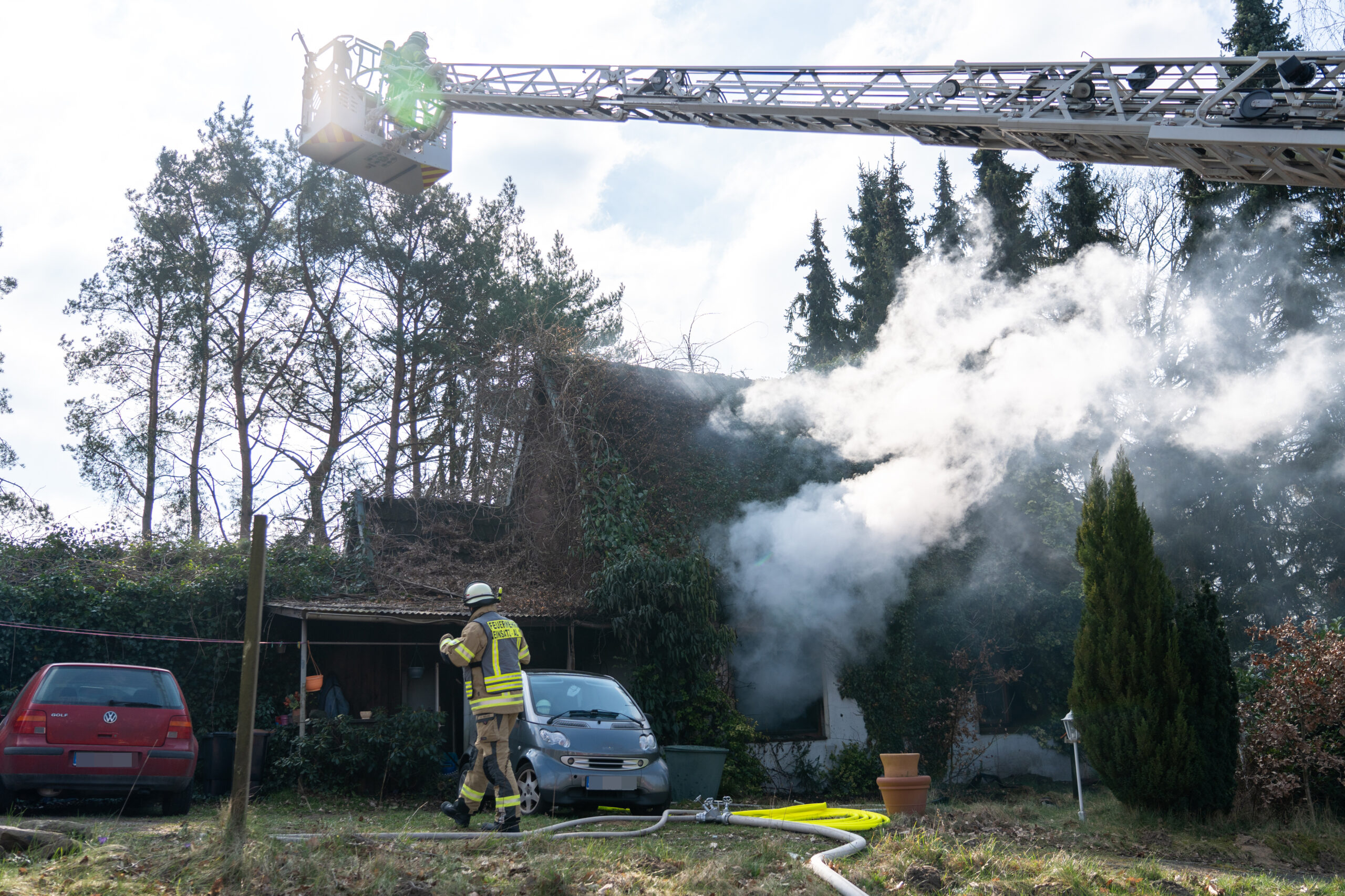 Qualm dringt aus dem Haus. Feuerwehrkräfte löschen vom Boden und von einer Drehleiter aus.