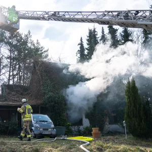 Qualm dringt aus dem Haus. Feuerwehrkräfte löschen vom Boden und von einer Drehleiter aus.