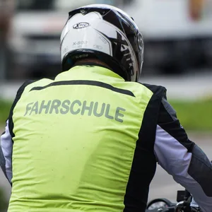 Ein Mann mit Helm und "Fahrschule" Weste auf einem Motorrad