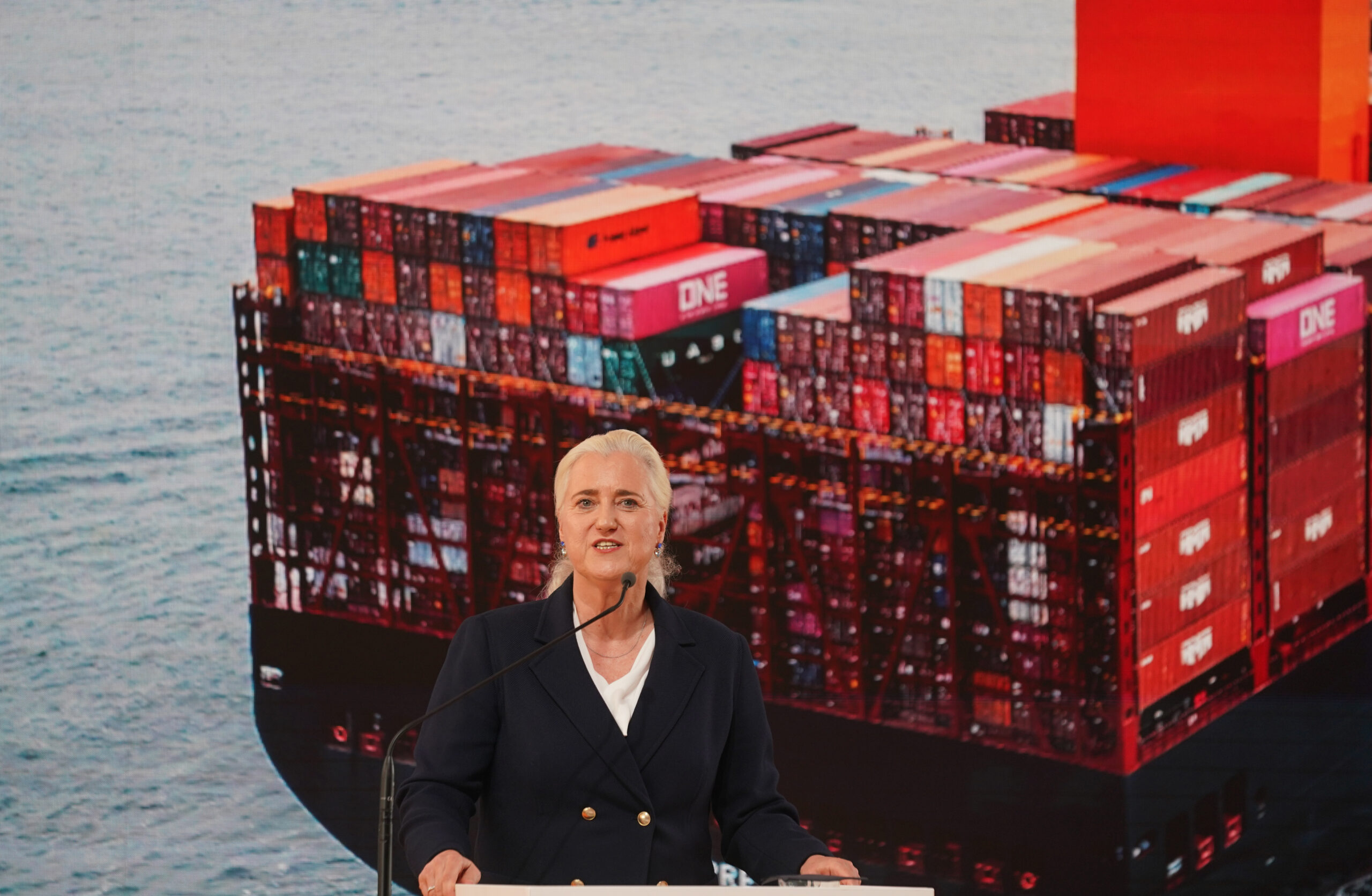 Blonde Frau vor einem Foto eines Containerschiffs