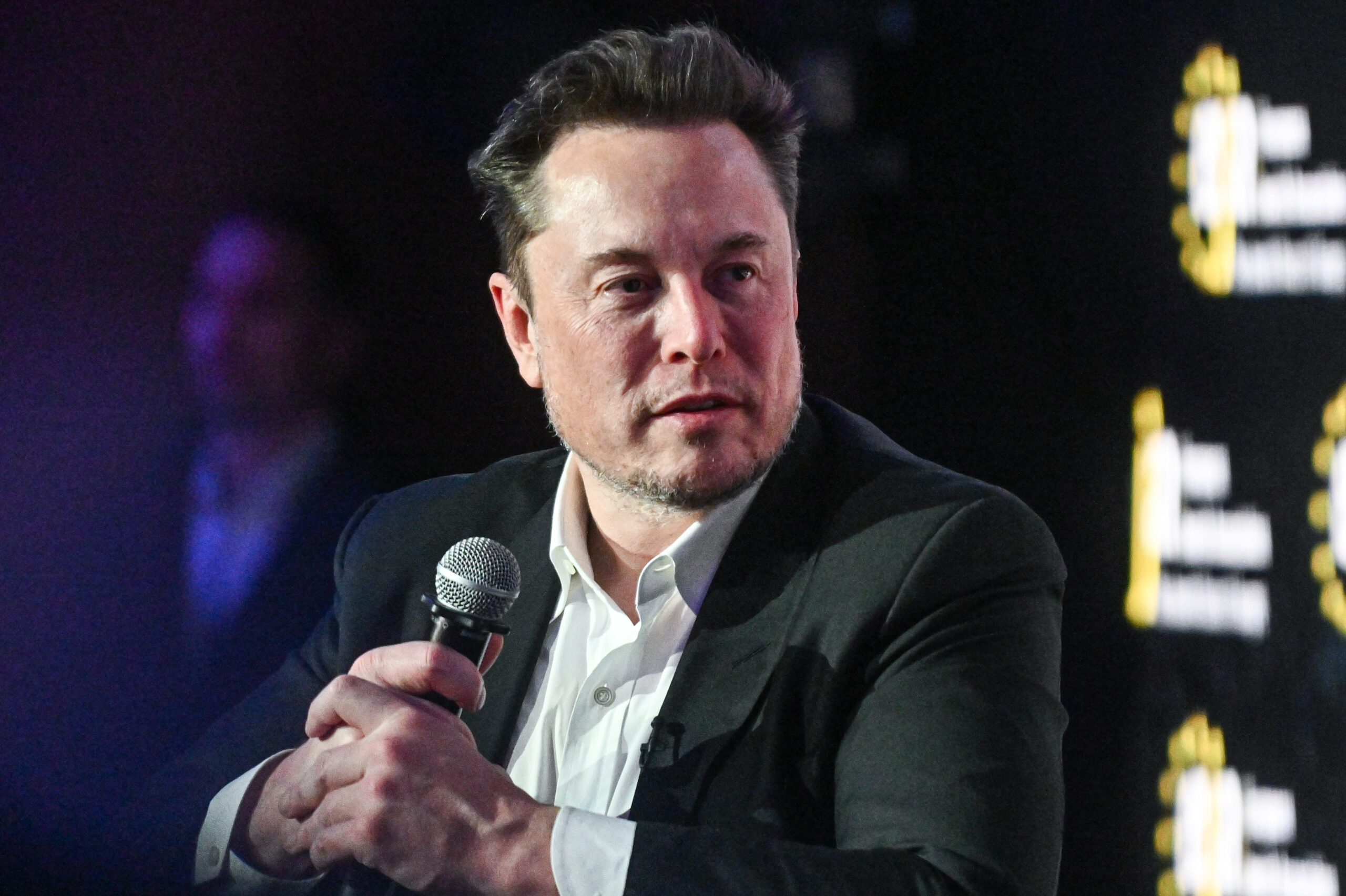 Elon Musk hält ein Mikrofon mit beiden Händen