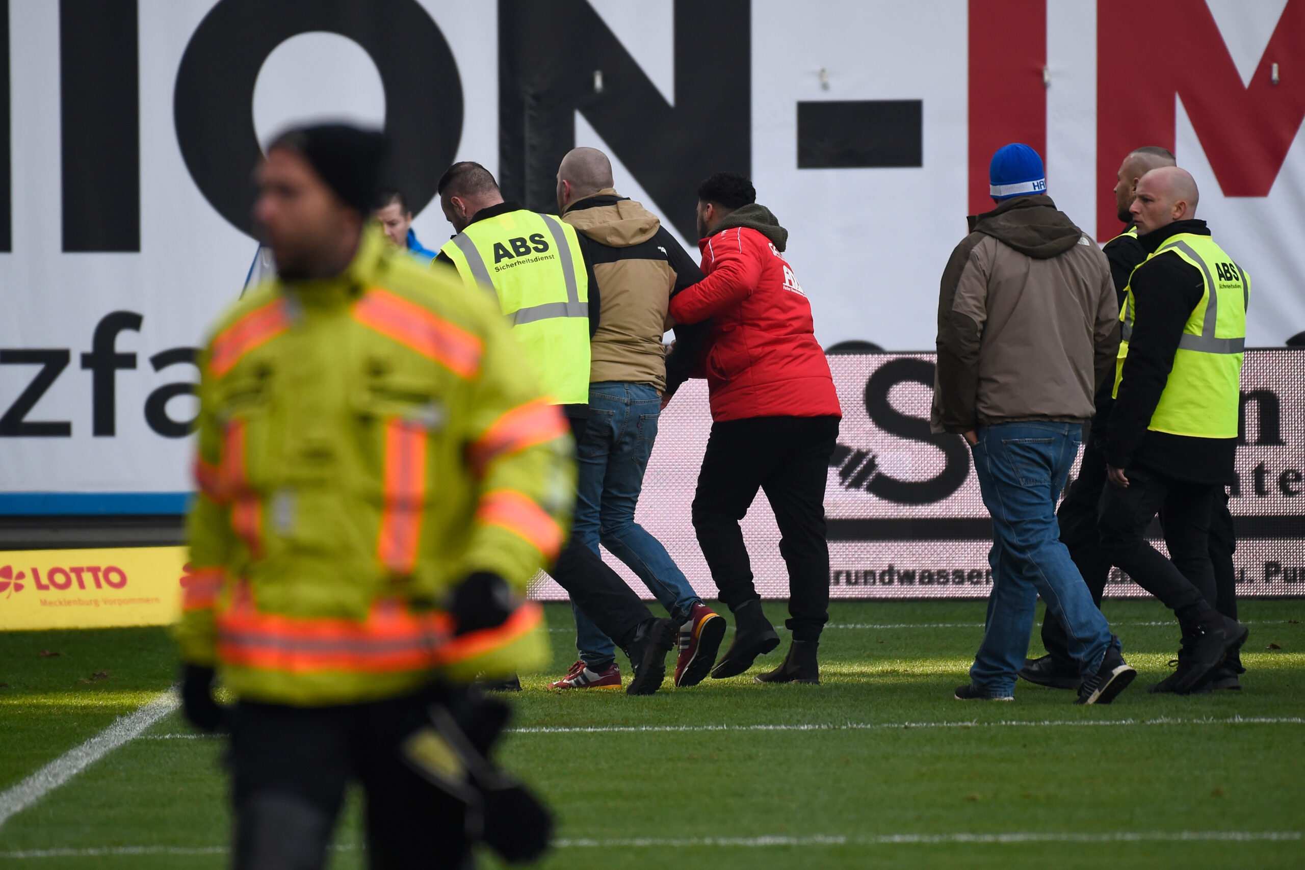Ein Rostock-Fan wird von Sicherheitskräften vom Spielfeld geführt.