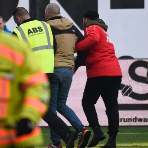 Ein Rostock-Fan wird von Sicherheitskräften vom Spielfeld geführt.