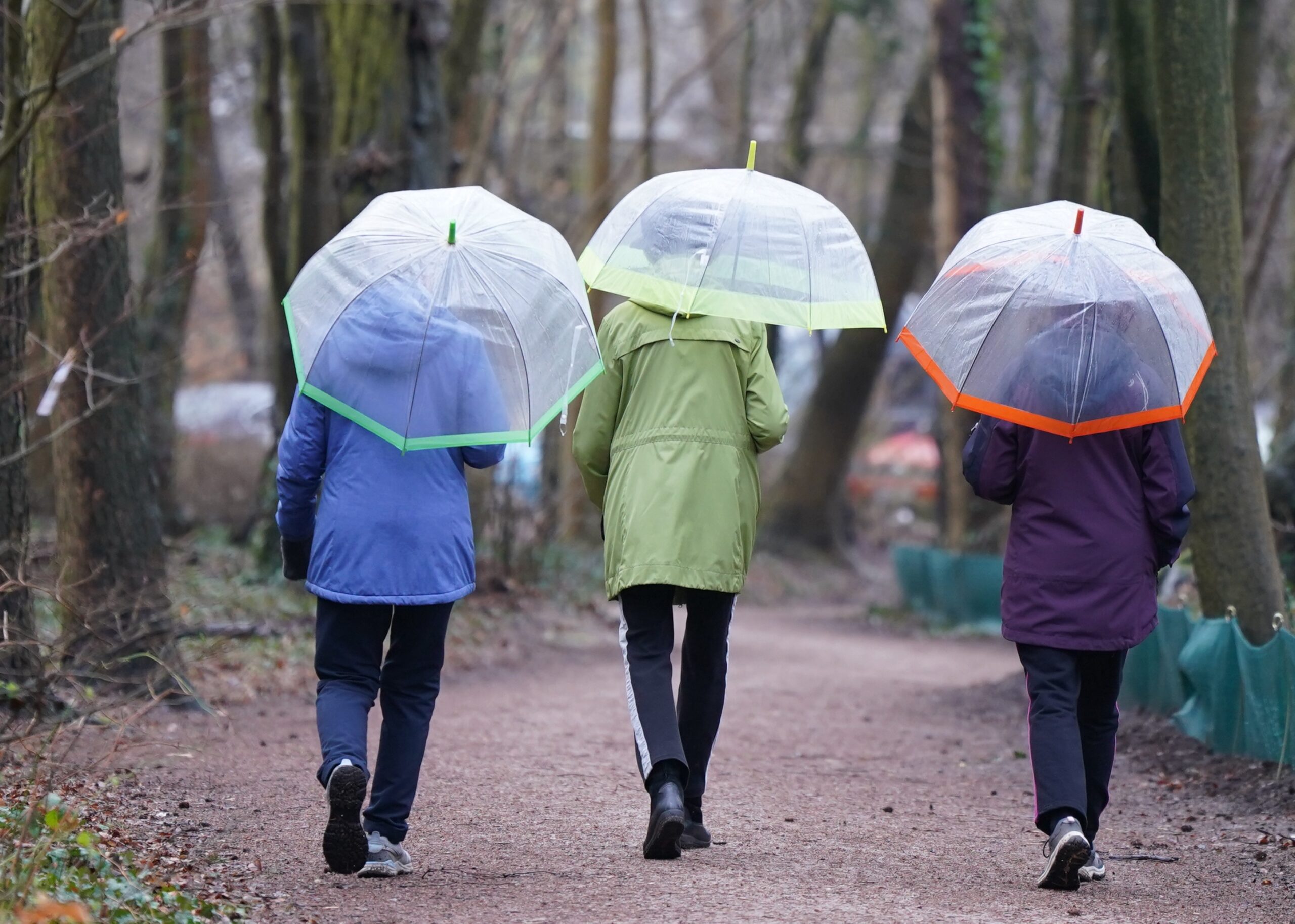 Drei Frauen gehen mit Regenschirmen spazieren.
