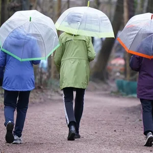 Drei Frauen gehen mit Regenschirmen spazieren.
