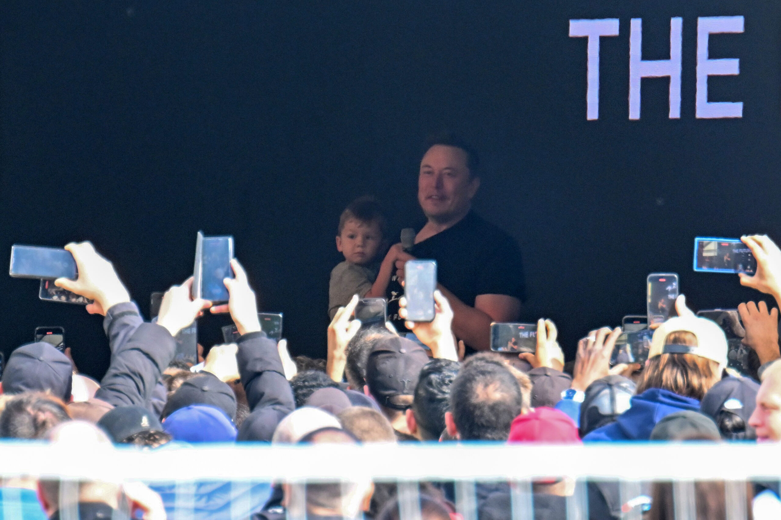 Tesla-Chef Elon Musk spricht in der Tesla Gigafactory Berlin-Brandenburg zu den Mitarbeitern und hält dabei ein Kind auf dem Arm.