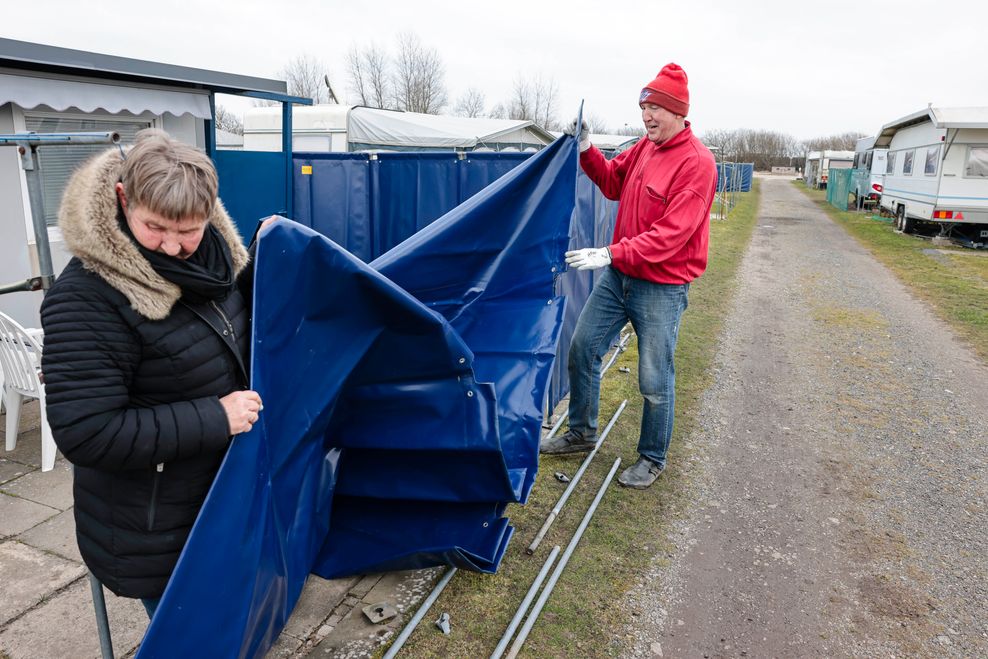Eggert (l) und Beate Raezke aus dem Kreis Pinneberg befestigen einen Windschutz vor einem Wohnwagen.
