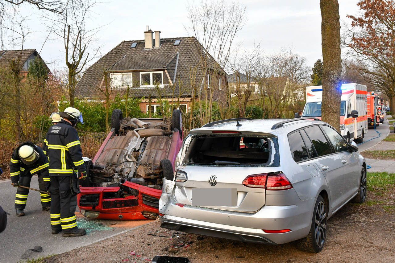 Ein roter Kleinwagen liegt demoliert auf dem Dach, davor stehen Feuerwehrleute.