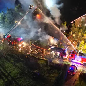 Großbrand in Oering: Luftaufnahme eines brennenden Einfamilienhauses, starker Qualm dringt aus dem Dach, davor Feuerwehrwagen, einer mit Drehleiter