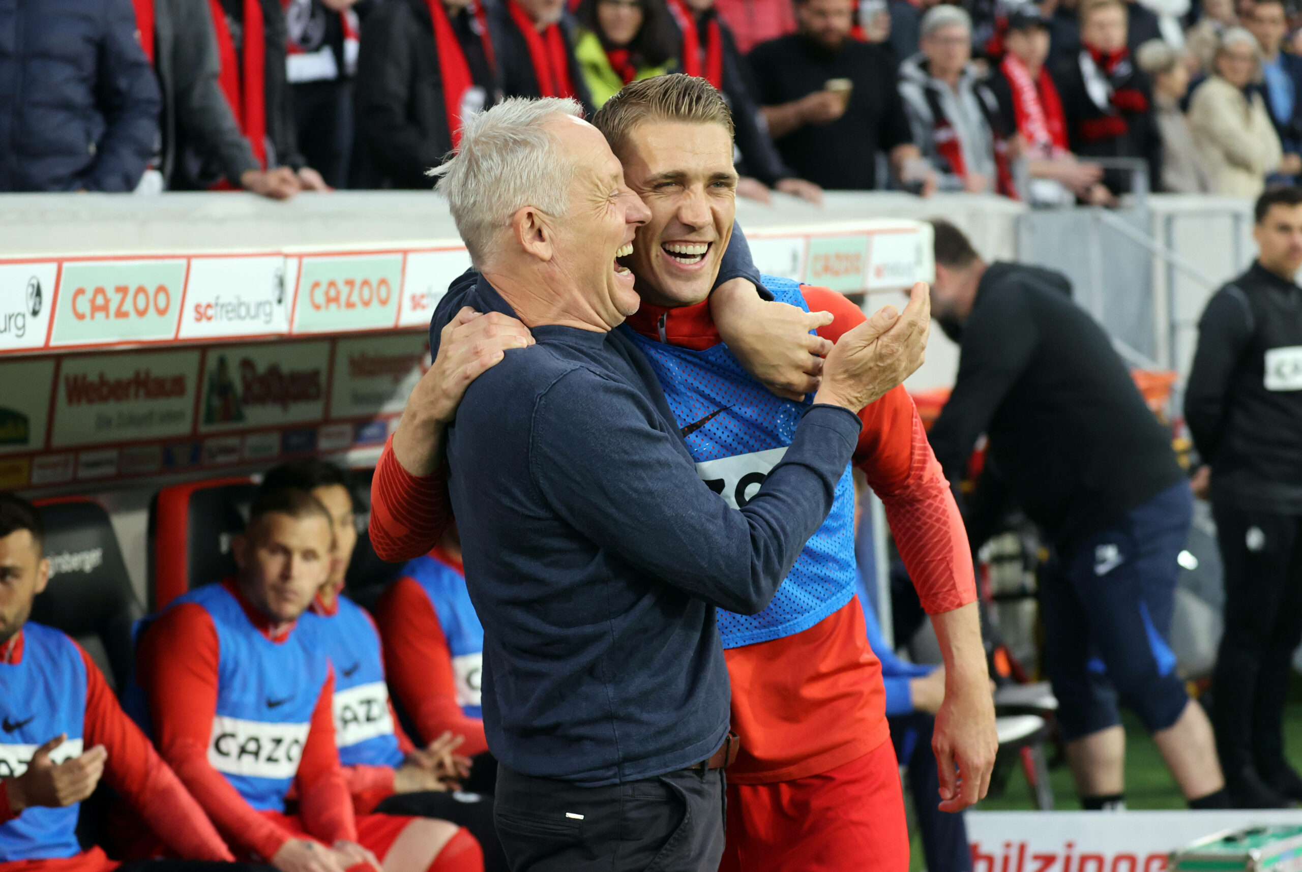 Christian Streich (l.) und Nils Petersen liegen sich lachend in den Armen an der Seitenlinie.
