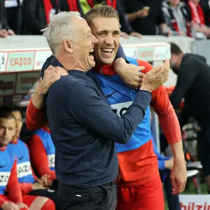 Christian Streich (l.) und Nils Petersen liegen sich lachend in den Armen an der Seitenlinie.