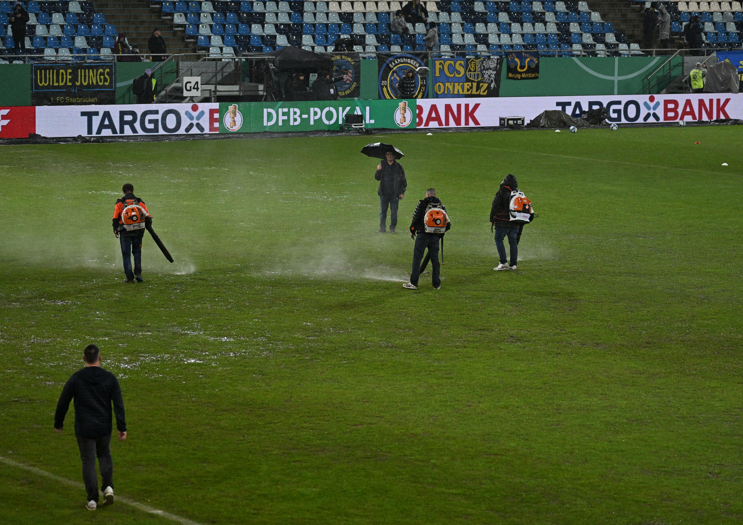 Helfer versuchen in Saarbrücken den Rasen kurz vor dem Spiel noch mit Laubbläsern zu retten.