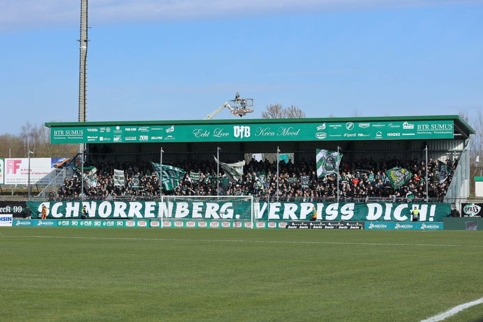 Ein großes Plakat ist am Fanblock befestigt, mit der Aufschrift: „Schnorrenberg, verpiss dich!“.