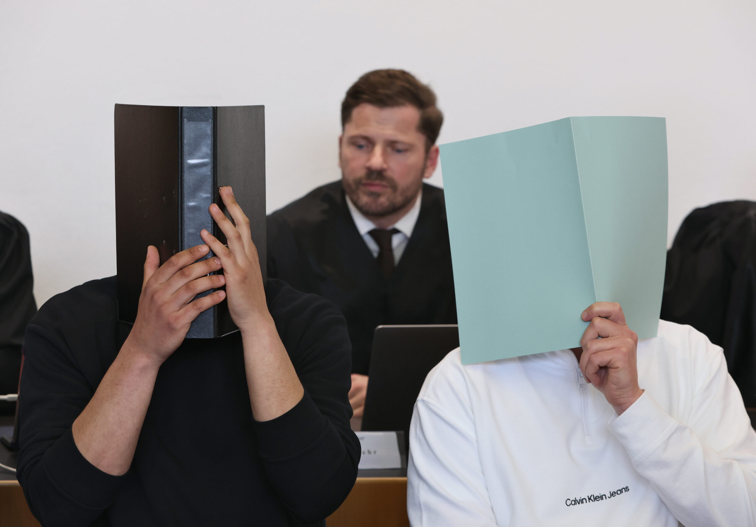 Die angeklagten Böllerwerfer verdecken vor Gericht ihre Gesichter.