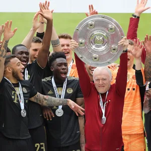 Hermann Gerland reckt die Meisterschale in die Höhe - das Team feiert um ihn herum.