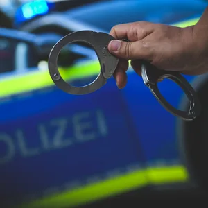Ein Polizist hält Handschellen vor einem Streifenwagen.
