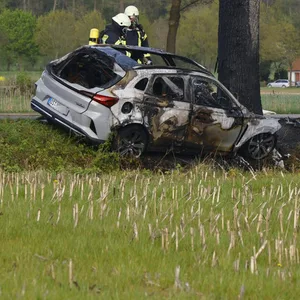 Feuerwehrleute sind an der Unfallstelle im Einsatz. Das Fahrzeug wurde durch den Brand völlig zerstört.