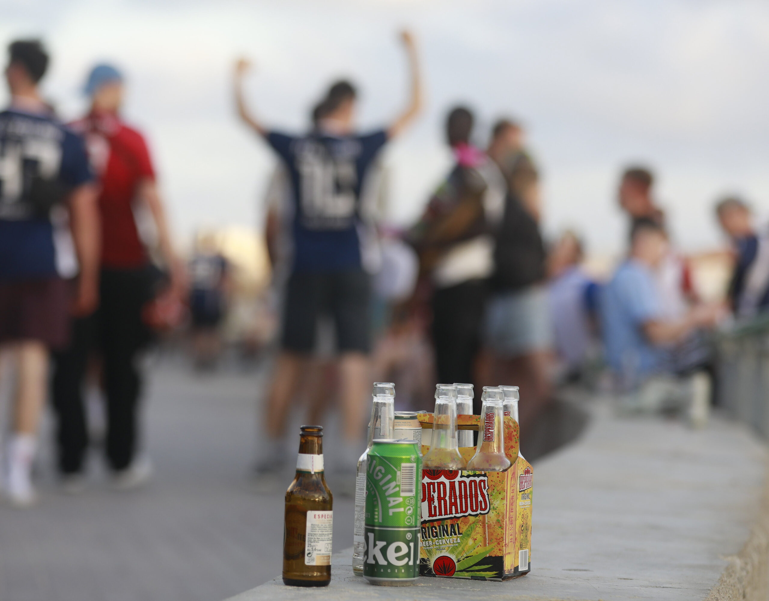 Menschen haben sich am Abend an der Promenade am Strand von Arenal versammelt. Auf einer Balustrade stehen mehrere leere Flachen alkoholischer Getränke.