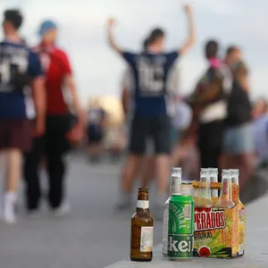 Menschen haben sich am Abend an der Promenade am Strand von Arenal versammelt. Auf einer Balustrade stehen mehrere leere Flachen alkoholischer Getränke.